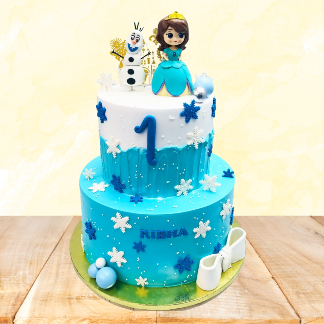 A two-tiered blue and white birthday cake decorated with snowflakes, featuring a figurine of Olaf from Frozen and a princess on top, with the name "RIBHA" written on the bottom tier.